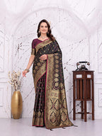A woman models a dark brown and gold Banarasi silk saree with a deep purple blouse, standing in front of a white arched wall decorated with a gold vase and a wooden side table.