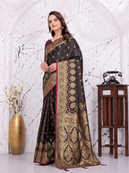 A woman models a dark brown and gold brocade saree with pink borders, standing in a white arched room with decorative props including a gold vase and a wooden table with a vintage telephone.