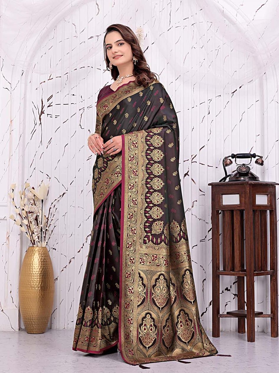 A woman models a dark brown and gold brocade saree with pink borders, standing in a white arched room with decorative props including a gold vase and a wooden table with a vintage telephone.