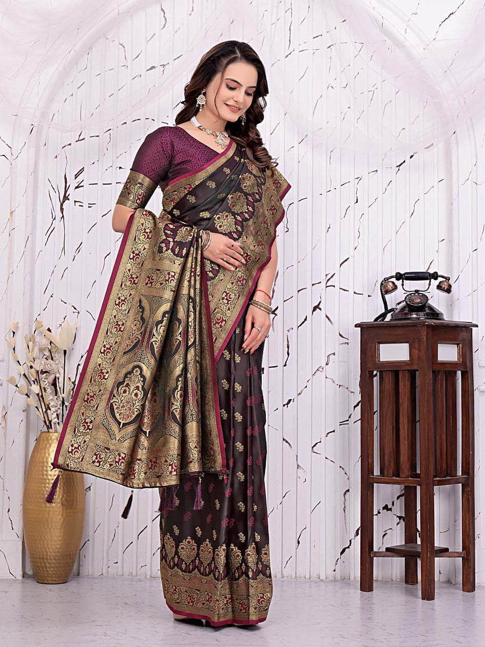 A woman models a traditional Indian saree in a decorated indoor setting with a white arched wall, a wooden table with a vintage telephone, and a gold vase. The saree has a dark purple and black base with intricate gold and red floral patterns.